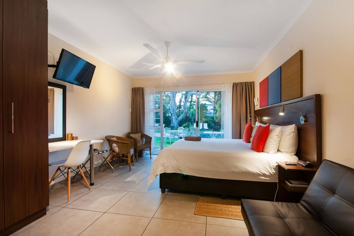Habitación de hotel con cama, escritorio con silla, televisión montada en la pared y ventilador de techo.