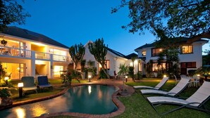 Una casa de dos pisos con piscina, mobiliario exterior y un patio bien iluminado.