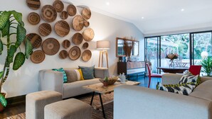 Una sala moderna con un gran panel de cestas tejidas, un sofá con cojines estampados, una mesa de centro con un cactus y vistas al exterior a través de amplios ventanales.