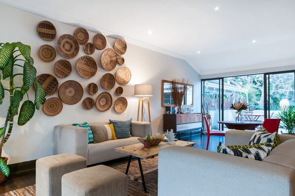 Una sala moderna con un gran panel de cestas tejidas, un sofá con cojines estampados, una mesa de centro con un cactus y vistas al exterior a través de amplios ventanales.