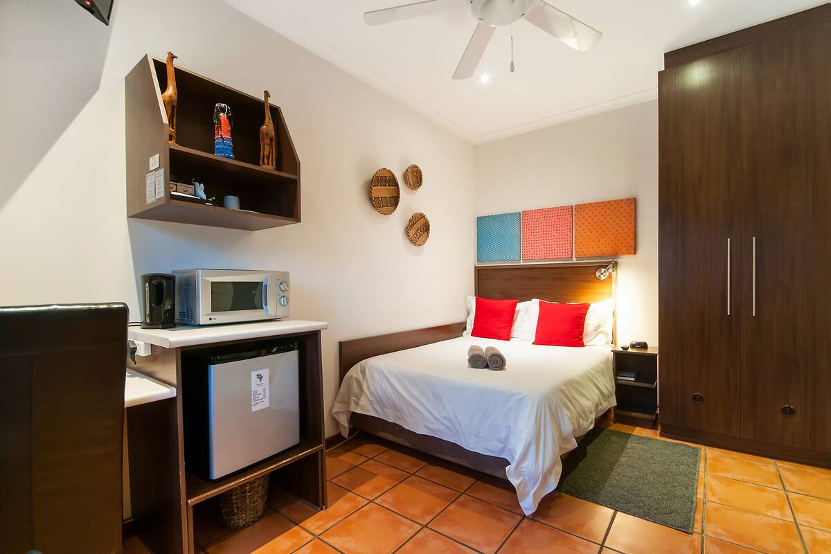 Habitación de hotel con cama, microondas, refrigerador pequeño, armario de madera y ventilador de techo.