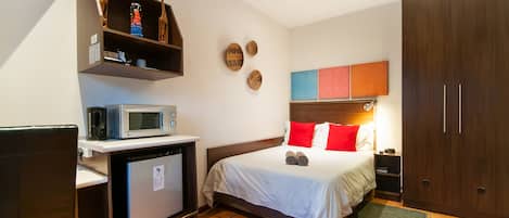 A hotel room with a bed, a microwave, a small refrigerator, a wooden cabinet, and a ceiling fan.
