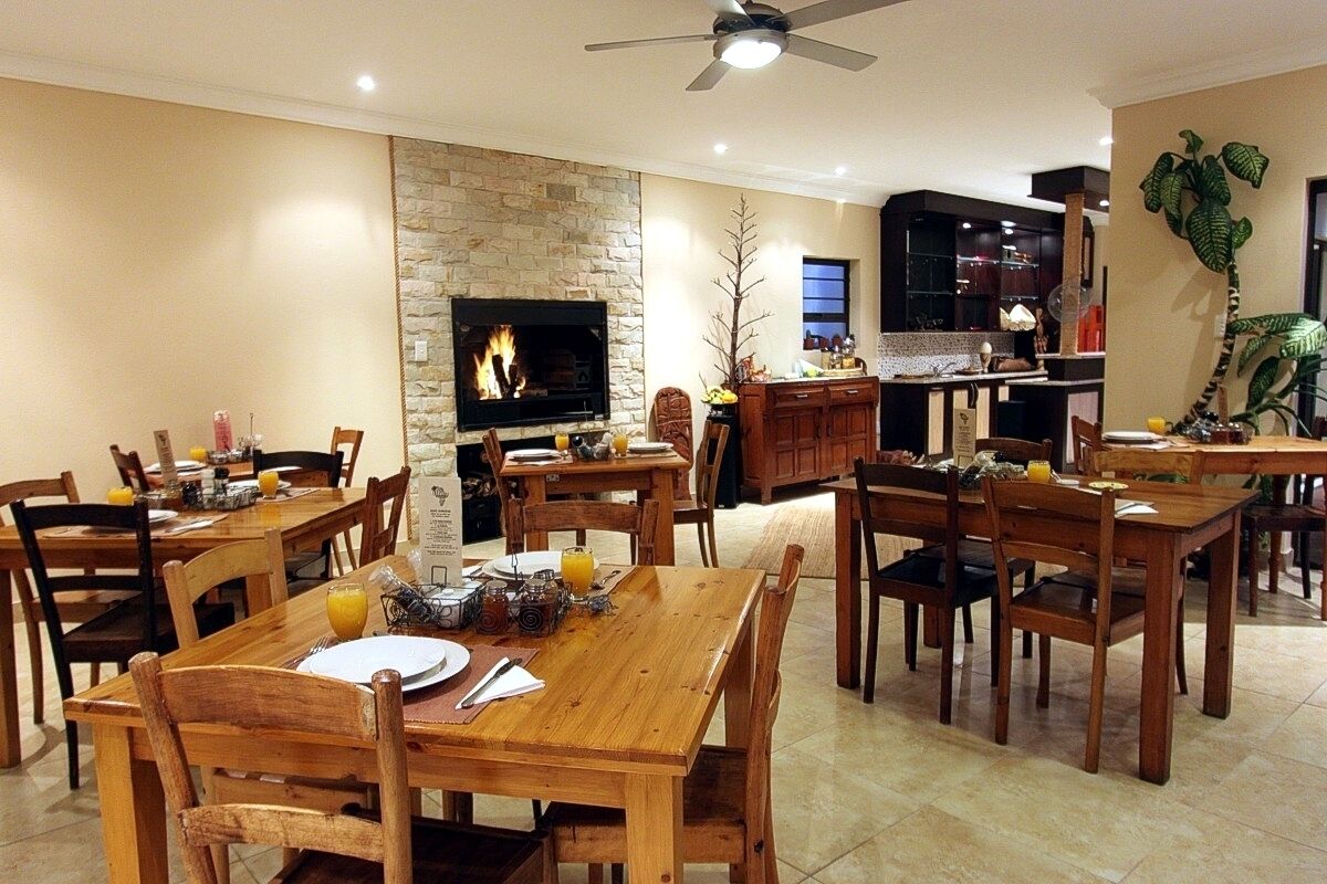A spacious dining area with wooden tables and chairs, a stone fireplace, and a modern kitchen in the background.