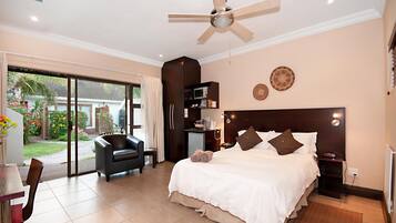 Habitación de hotel con cama, escritorio, silla, ventilador de techo y vista al exterior.