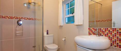 A bathroom with a glass shower enclosure, a toilet, a sink with a mirror, and a window with curtains.