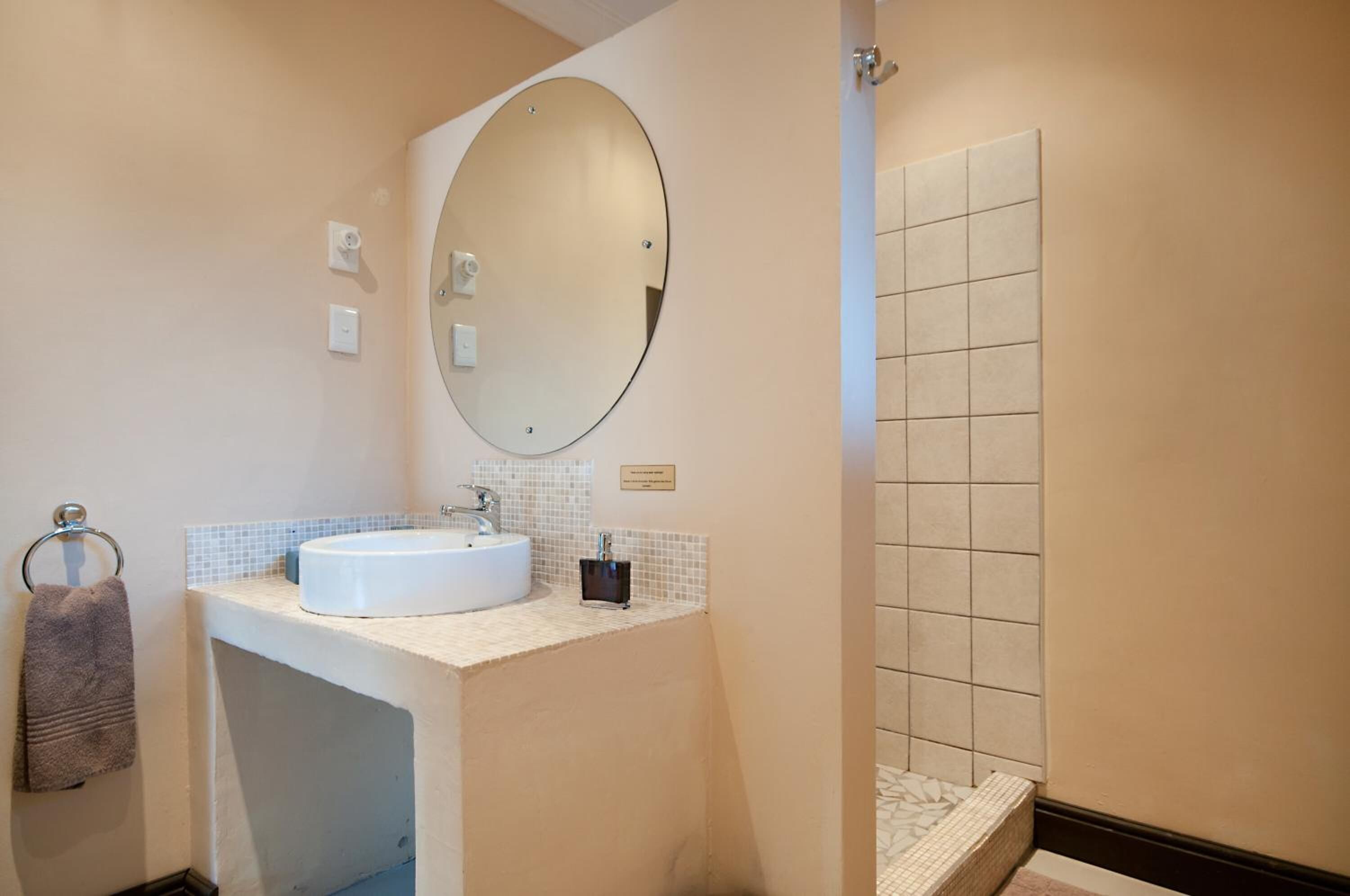 A bathroom with a white sink, a round mirror, a towel rack, and a tiled shower area.