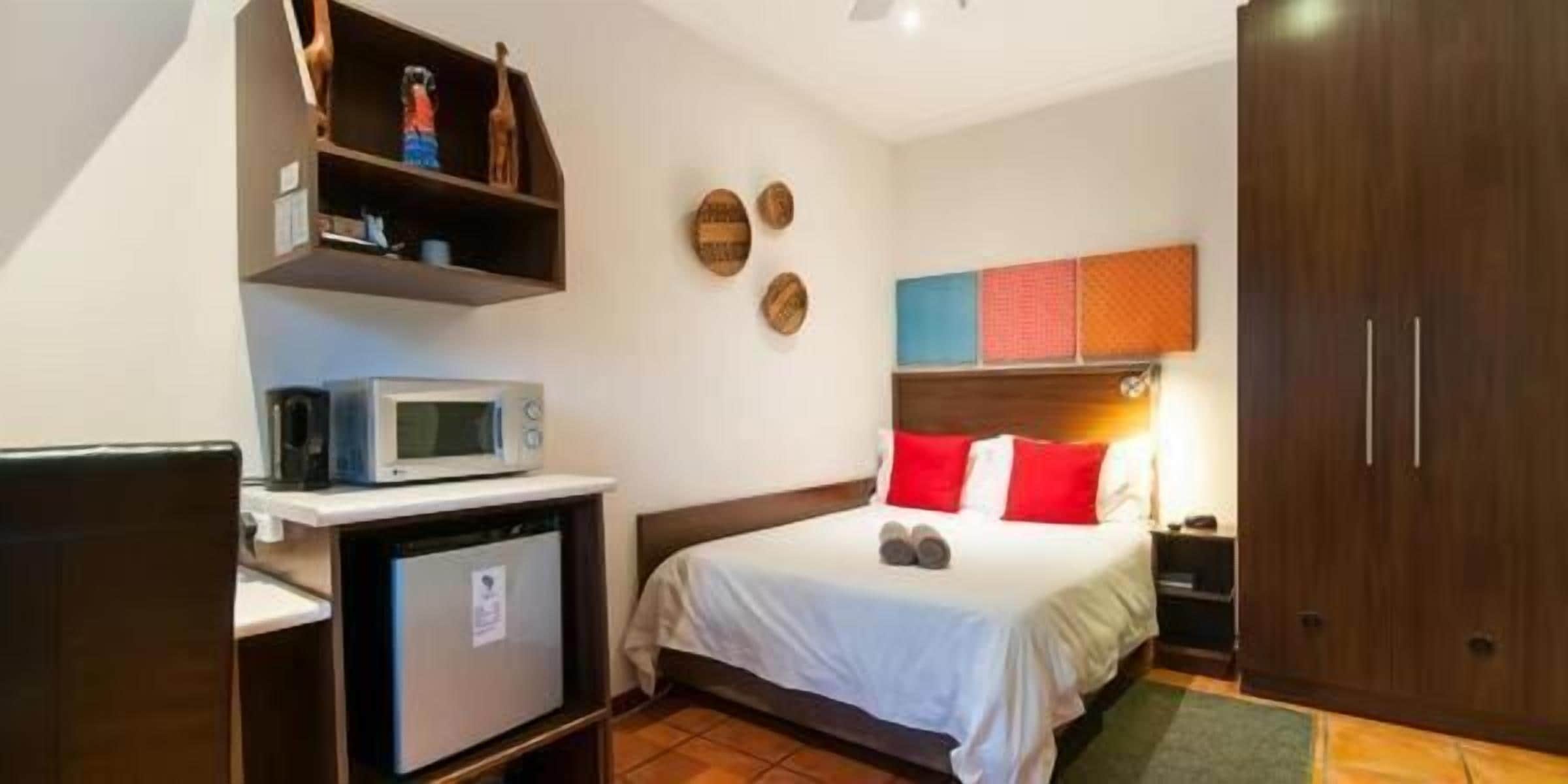 Een hotelkamer met een bed, een magnetron, een kleine koelkast, een bureau en een kledingkast.