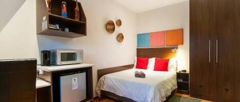 A hotel room with a bed, a microwave, a small refrigerator, a desk, and a wardrobe.