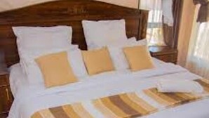 A neatly made bed with white and beige bedding, a wooden headboard, and a striped throw blanket.