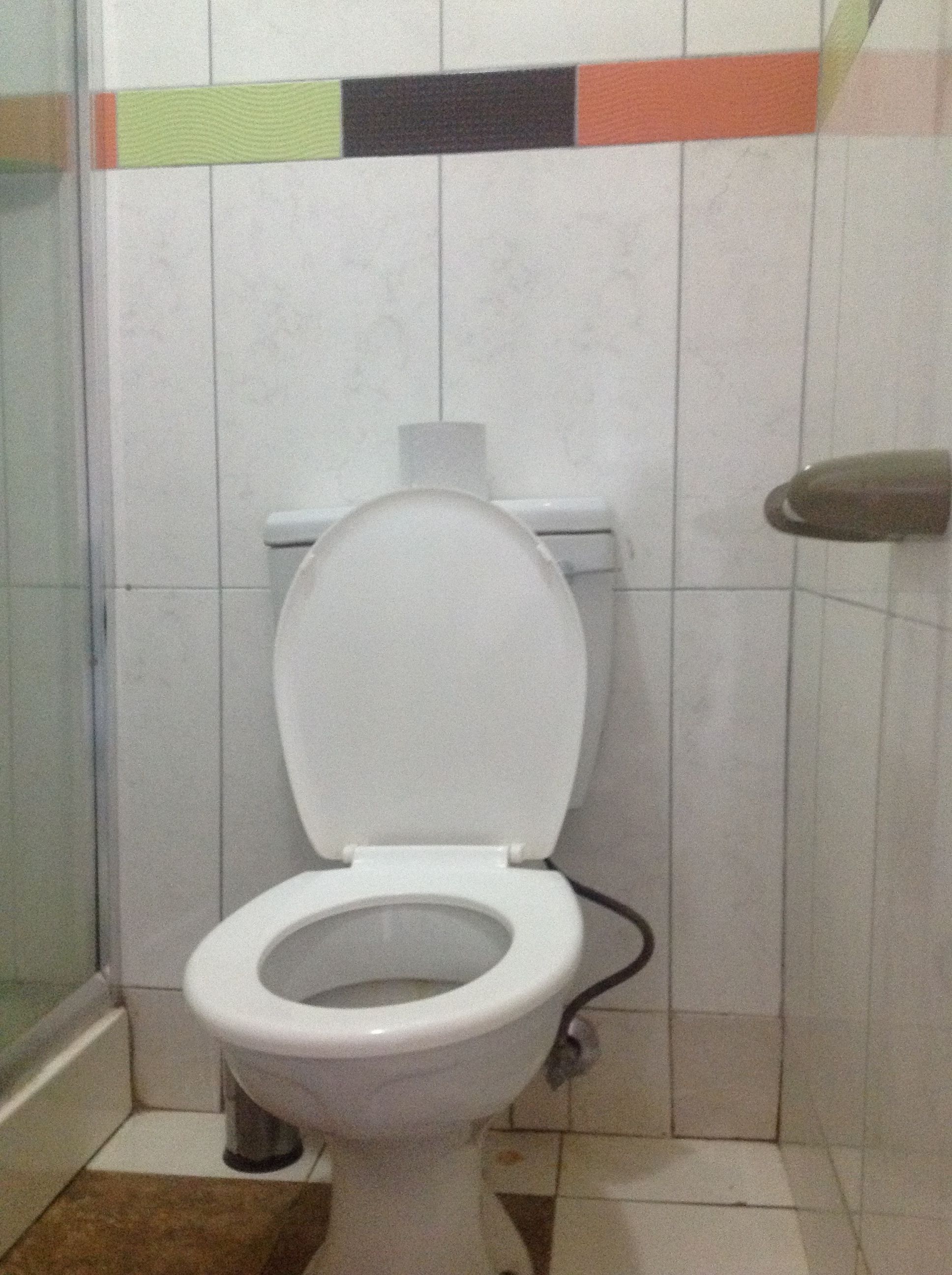 A standard white toilet in a bathroom with tiled walls and a visible pipe on the floor.