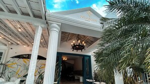 Fachada de hotel blanca, con columnas, una araña y asientos al aire libre.