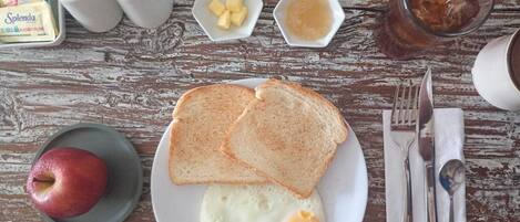 A breakfast plate with toast, eggs, and an apple, along with condiments and a glass of iced tea on a wooden table.