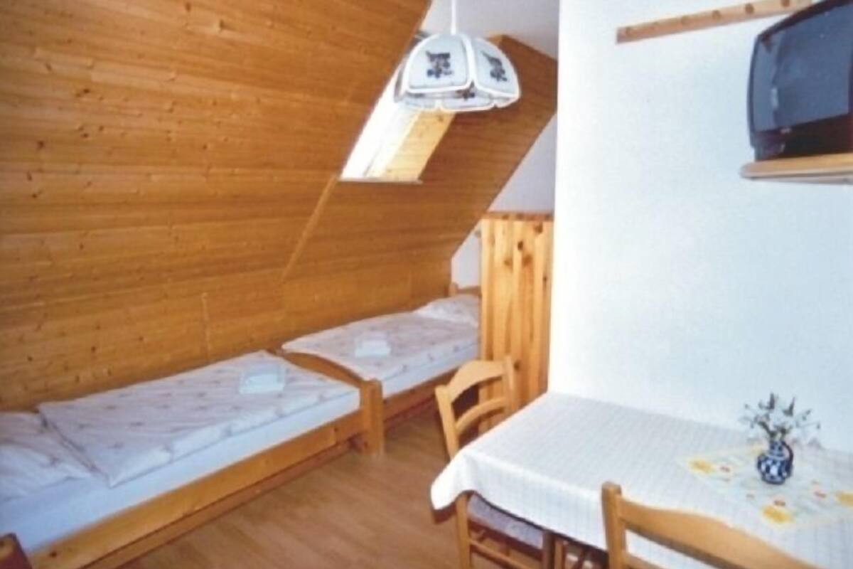 Ein kleiner, gemütlicher Raum mit Holzwänden und einer schrägen Decke. Zwei Einzelbetten und ein Tisch mit einem Blumenstrauß sind vorhanden.
