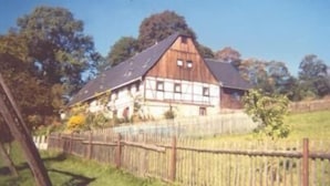 Une maison en bois avec un toit en pente, entourée d’une clôture en bois et d’arbres.