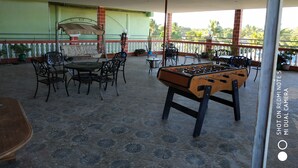 Un espace extérieur aménagé avec des tables et des chaises, un baby-foot et une vue sur la verdure.