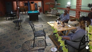 Une table de billard, une table de jeu de flipper et un coin repas avec des chaises et une table dressée pour deux personnes.