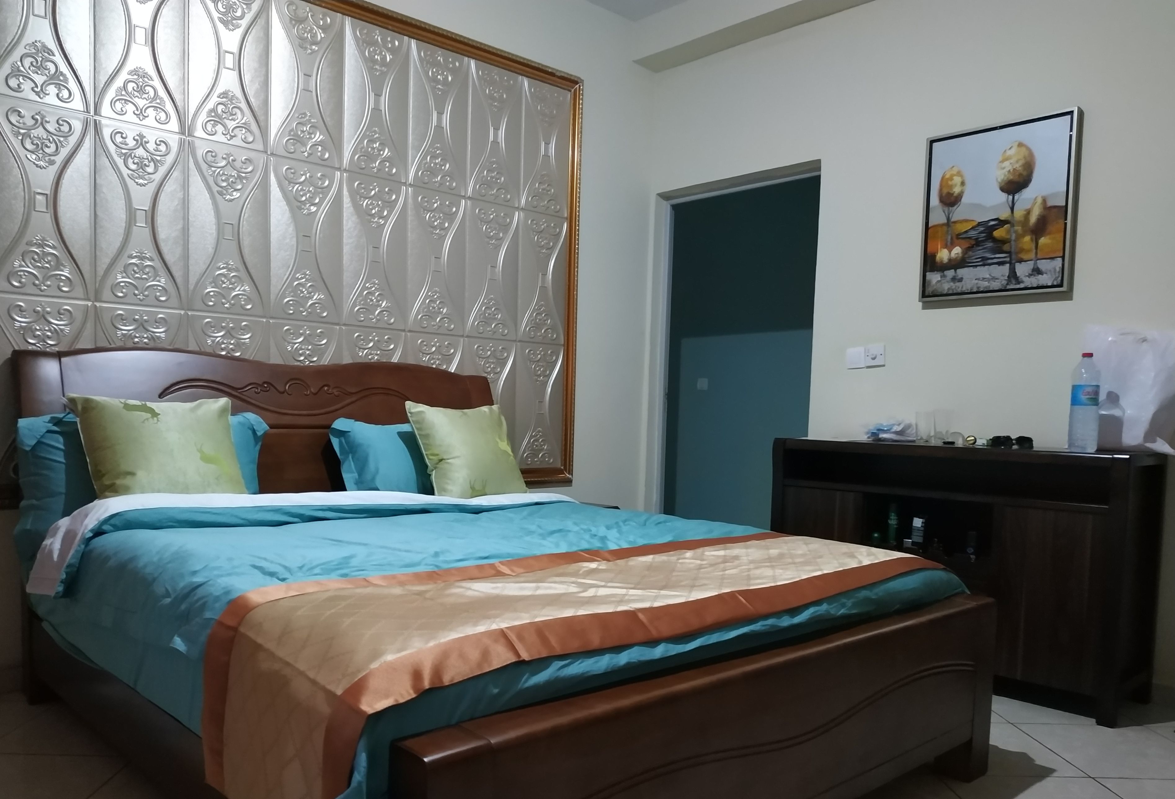 A bedroom with a bed, a wooden headboard, a nightstand, a painting, and a door.