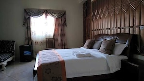 Une chambre à coucher comprenant un lit, une table de chevet, une chaise, un téléviseur et une fenêtre avec des rideaux.