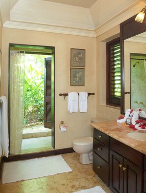 A bathroom with a toilet, sink, and towel rack. There is a window with a view of greenery outside.