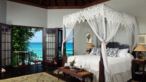 A four-poster canopy bed with a view of the ocean, a wooden chair, a small table with a bottle and glasses, and a nightstand with a lamp. - Bluefields Bay Villas (Bluefields)