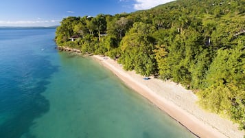 Uma praia com águas turquesa cristalinas, areal arenoso e vegetação verde exuberante.