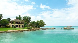 A beachfront property with a large house, palm trees, and a clear view of the ocean. - Bluefields Bay Villas (Bluefields)