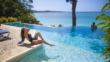 Área da piscina com vista para o mar, uma espreguiçadeira e uma pessoa relaxando.