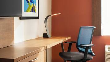 A modern office desk with a chair, a desk lamp, and a framed abstract artwork on the wall.