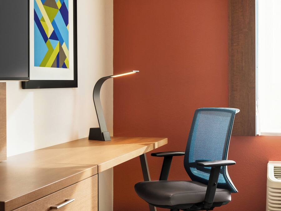 A modern office desk with a chair, a desk lamp, and a framed abstract artwork on the wall.