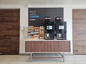 A coffee station with two espresso machines, a coffee dispenser, and a sign that reads 'MUST. HAVE. COFFEE.'