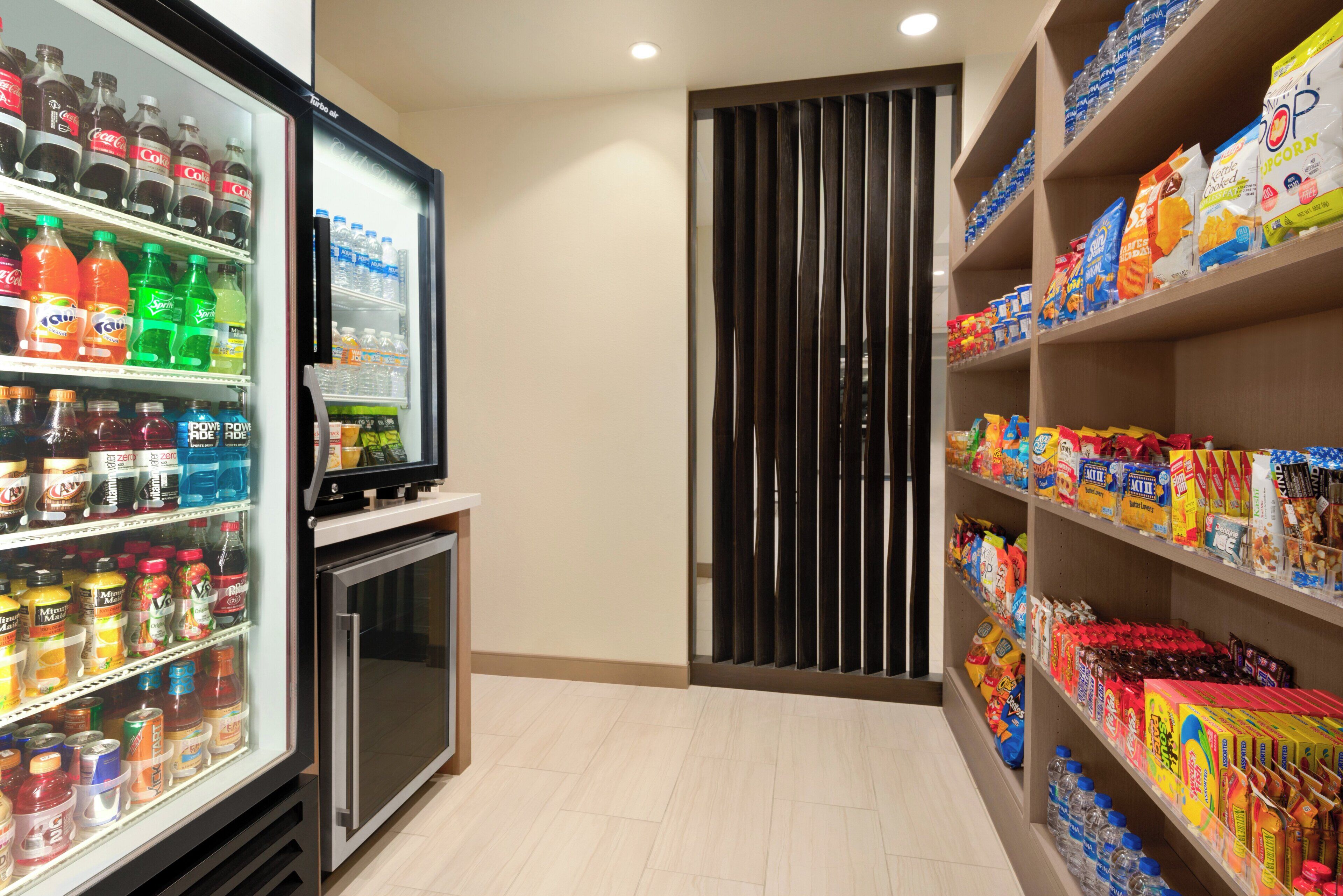 Un refrigerador para bebidas repleto de diversas opciones, junto a estantes con diferentes productos empacados.