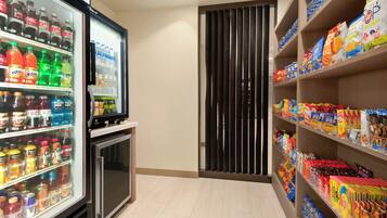 Un refrigerador para bebidas repleto de diversas opciones, junto a estantes con diferentes productos empacados.