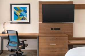 Quarto de hotel moderno com uma escrivaninha de madeira, televisão de tela plana, pintura abstrata emoldurada e cadeira de escritório de tela azul.
