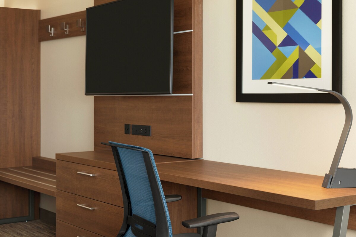 Uma mesa de escritório moderna com monitor de tela plana, uma cadeira de escritório azul e um quadro abstrato na parede.