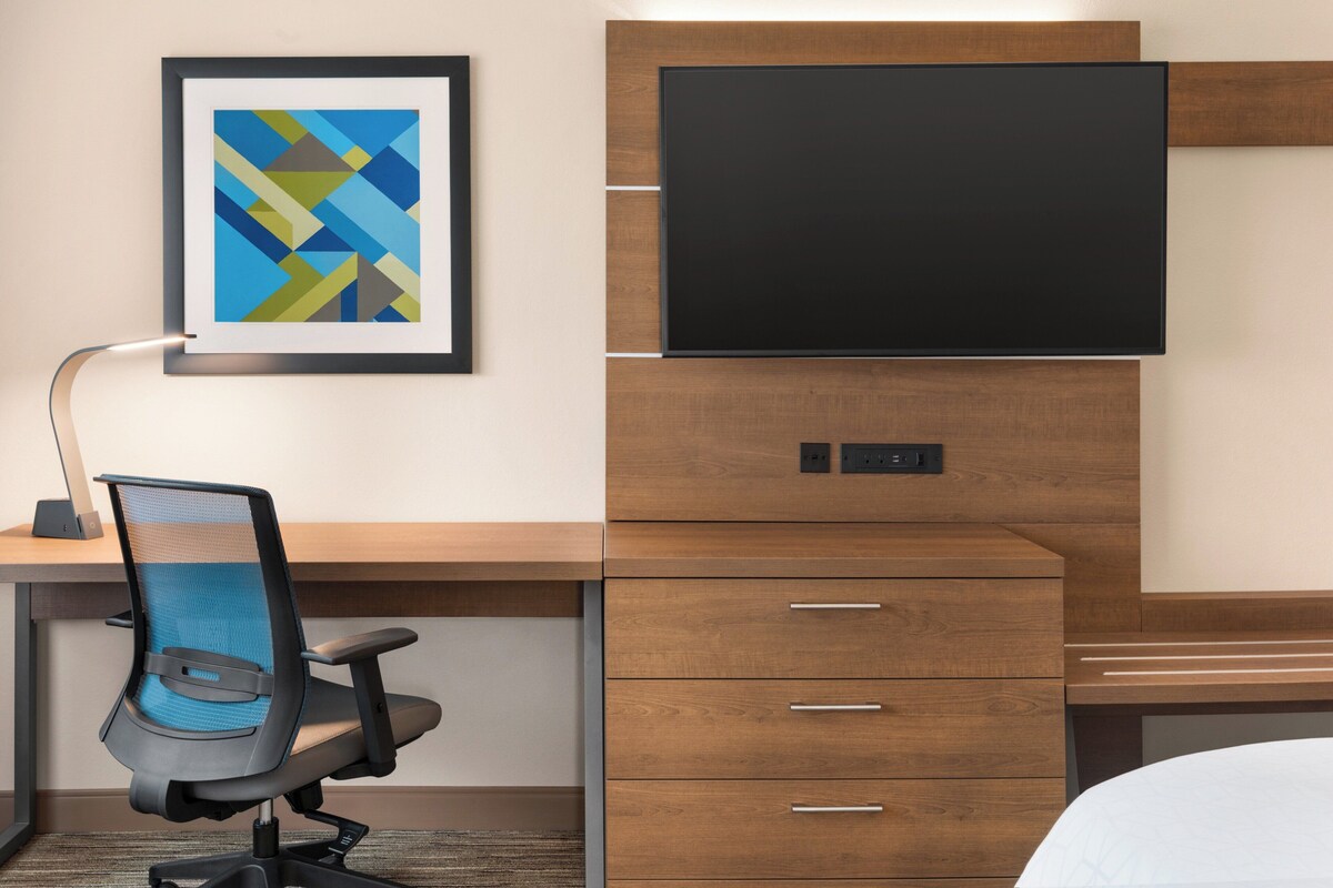 Quarto de hotel com escrivaninha, cadeira, televisão de tela plana, quadro decorativo e cama.