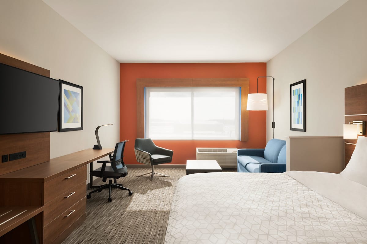 A hotel room with a bed, desk, chair, sofa, and a large window.