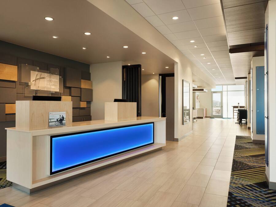 A modern hotel reception area with a long reception desk, a digital display, and a wall-mounted sign.