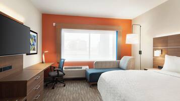 A hotel room with a bed, desk, chair, air conditioning unit, and a large window.