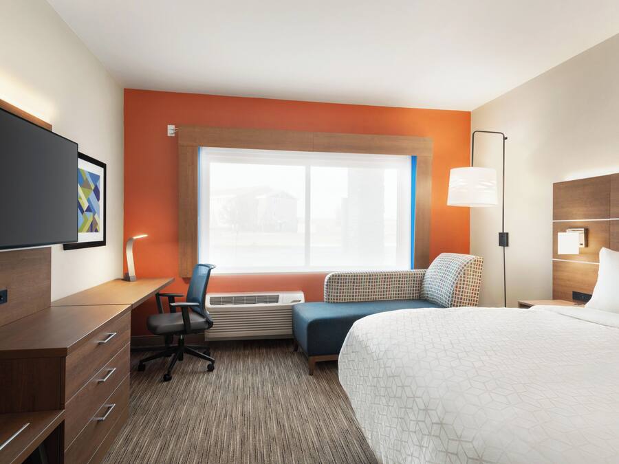 A hotel room with a bed, desk, chair, air conditioning unit, and a large window.