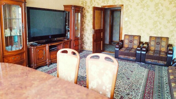 A traditional living room with a television, wooden furniture, patterned carpet, and a dining table. - Welcome Home 7 (Tashkent)