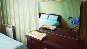 A room with a wooden dresser, a mirror reflecting a bed with blue bedding, and a radiator on the wall. - Welcome Home 7 (Tashkent)