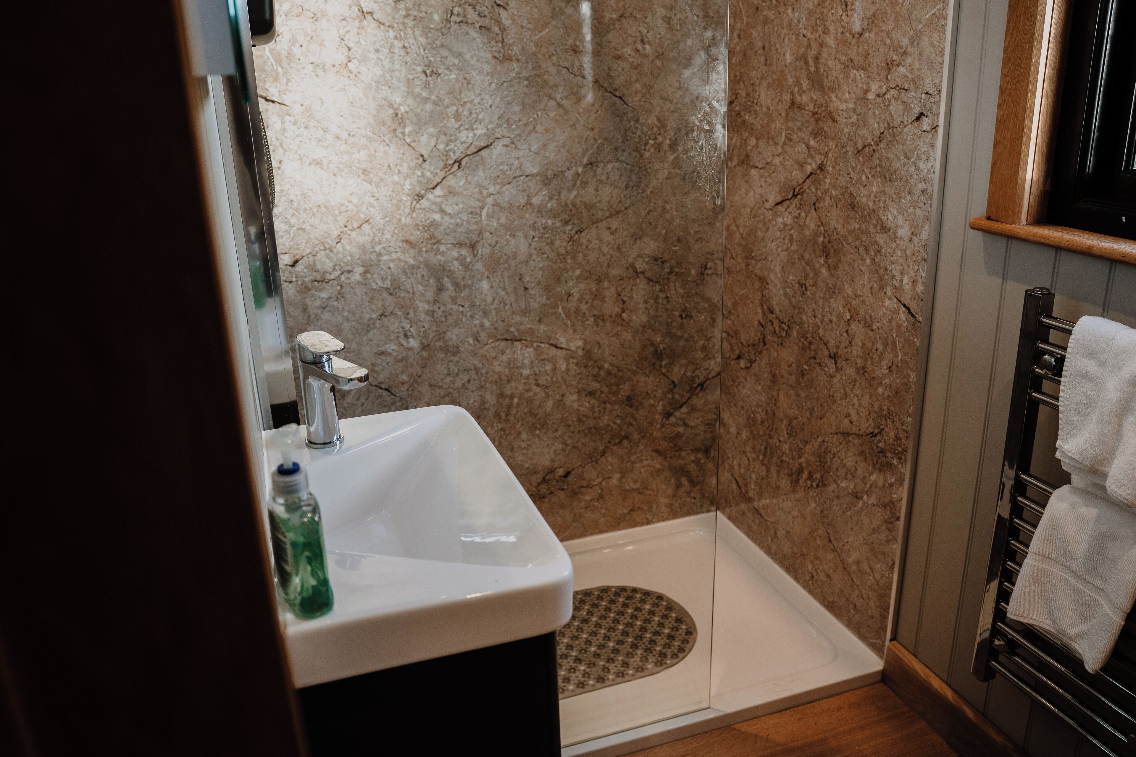A bathroom with a marble wall, a sink, a shower, and a towel rack.