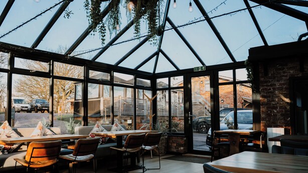 A restaurant with a glass roof, wooden tables, and chairs. - Rylands Farmhouse (Wilmslow)