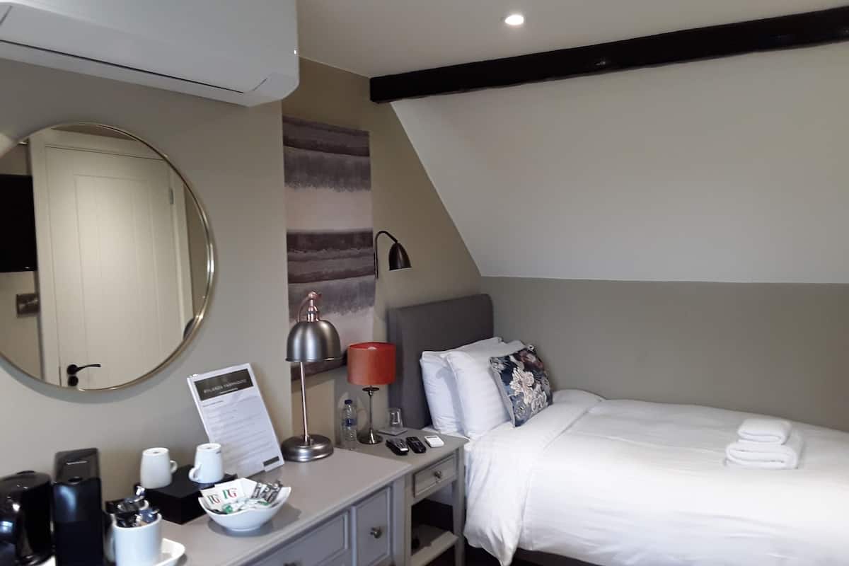 Une chambre d’hôtel comprenant un lit, un bureau avec un miroir, une lampe, un téléphone et une petite table avec une machine à café et des tasses.