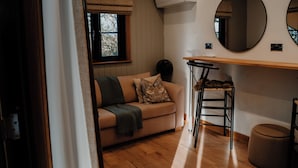 A cozy room with a wooden floor, a beige sofa with a throw blanket, a small round table, and a round mirror on the wall. - Rylands Farmhouse (Wilmslow)