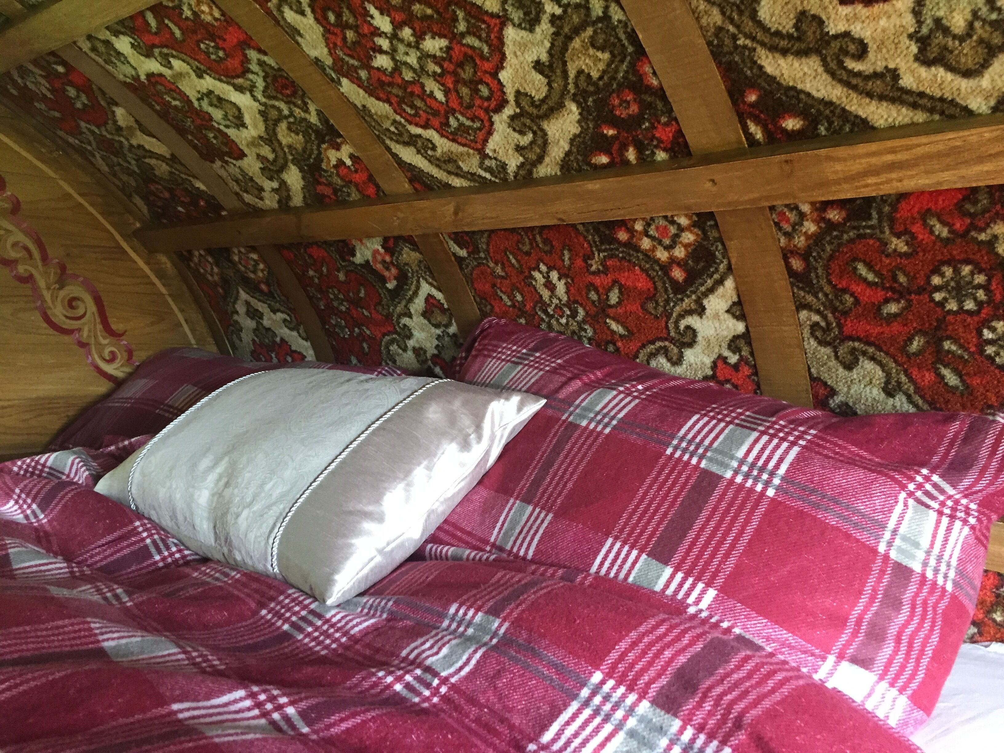 A bed with a plaid blanket and a pillow in a room with wooden beams and patterned wallpaper.