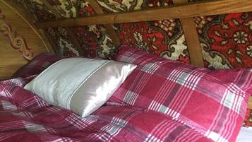 A bed with a plaid blanket and a pillow in a room with wooden beams and patterned wallpaper.