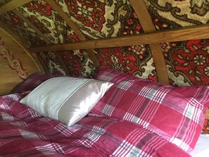 A bed with a plaid blanket and a pillow in a room with wooden beams and patterned wallpaper.