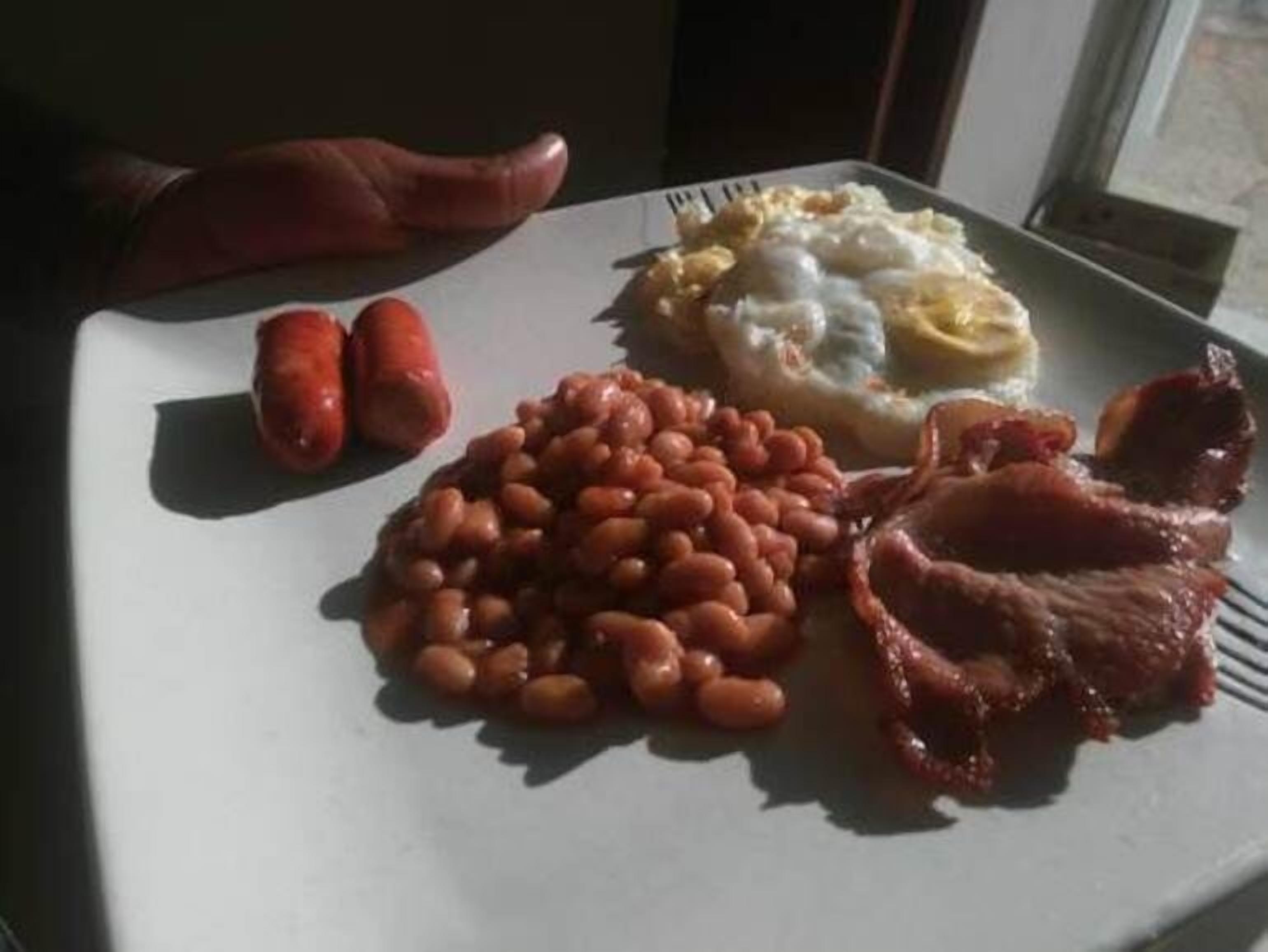 Un plato con salchichas, frijoles, tocino y huevos revueltos.