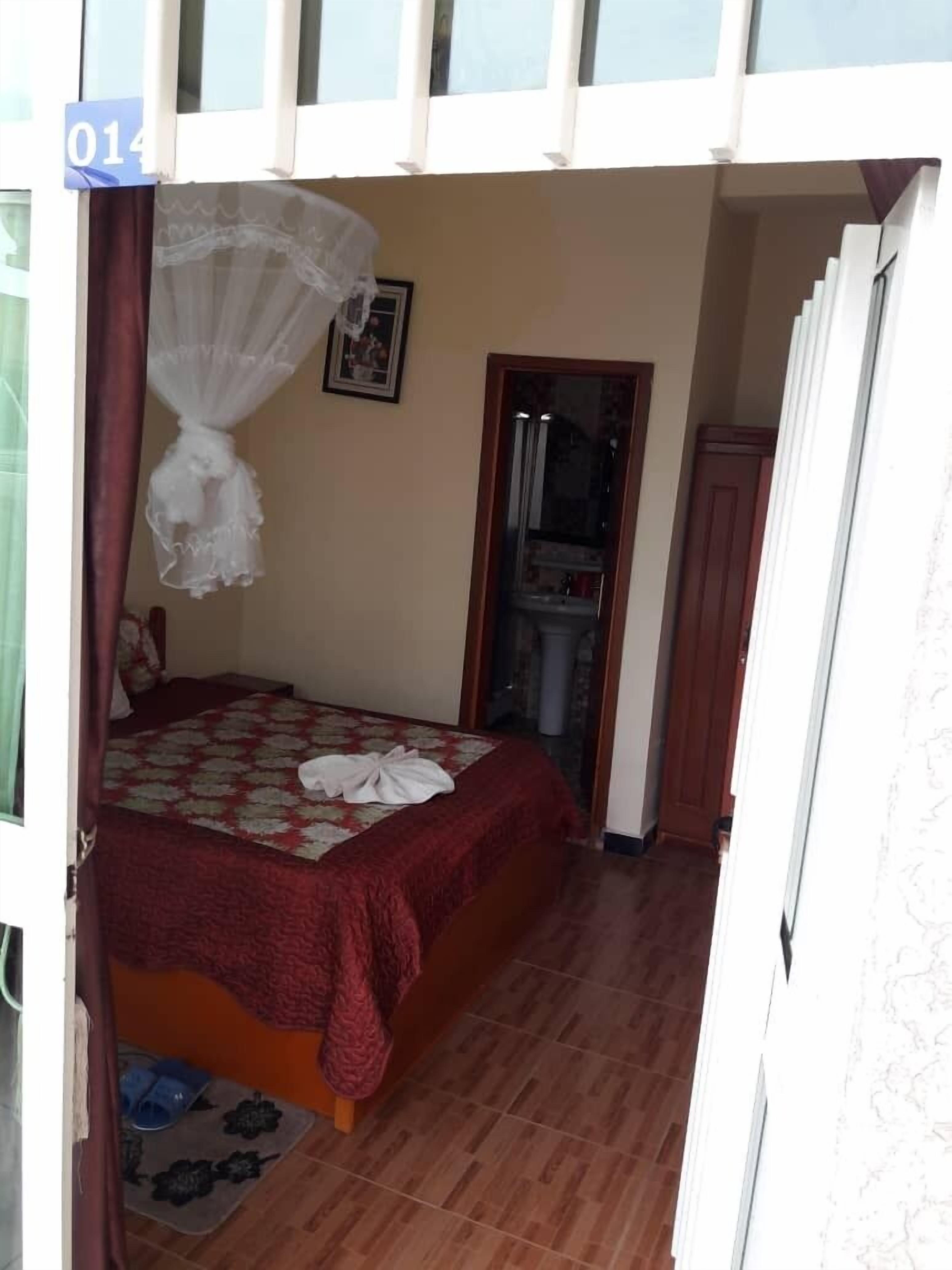 A bedroom with a bed, a window with curtains, a door, and a small bathroom visible through the door.